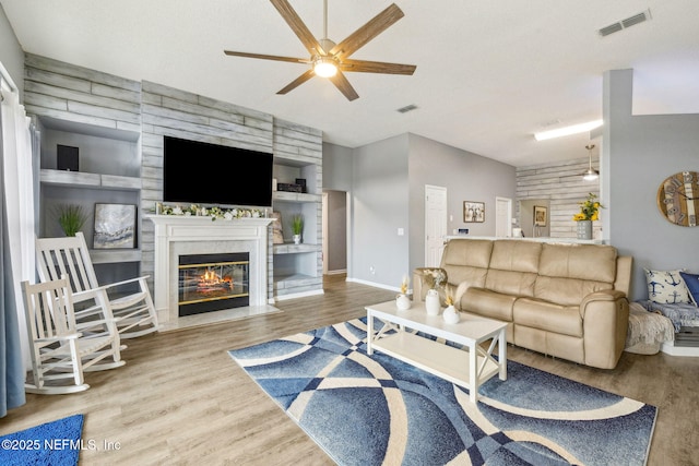 living room with built in features, ceiling fan, wood finished floors, and a fireplace