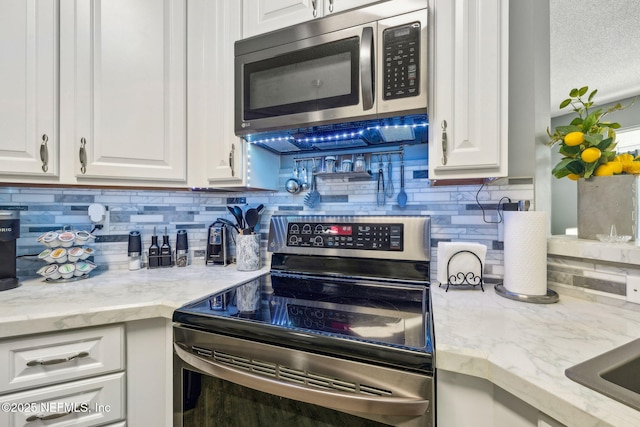 kitchen with white cabinets, light stone countertops, appliances with stainless steel finishes, and tasteful backsplash