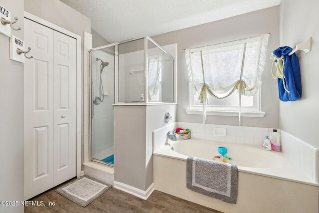 full bath featuring a garden tub, a textured ceiling, a shower stall, wood finished floors, and a closet