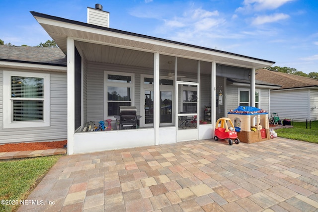 rear view of house with a shingled roof, a chimney, and a sunroom
