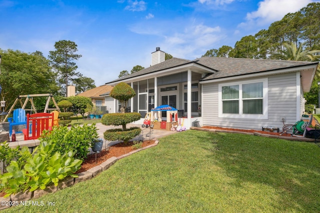 back of property with roof with shingles, a yard, a chimney, and a sunroom