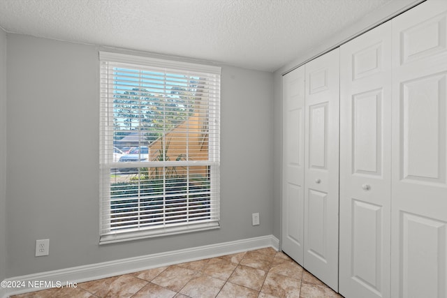 unfurnished bedroom with a textured ceiling, a closet, baseboards, and light tile patterned floors