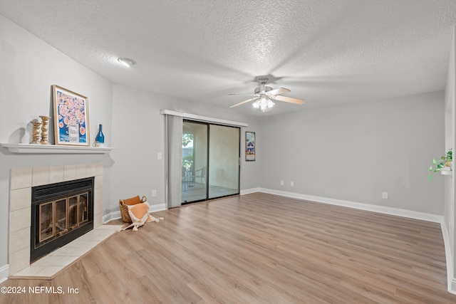 unfurnished living room featuring wood finished floors, a tiled fireplace, a textured ceiling, a ceiling fan, and baseboards