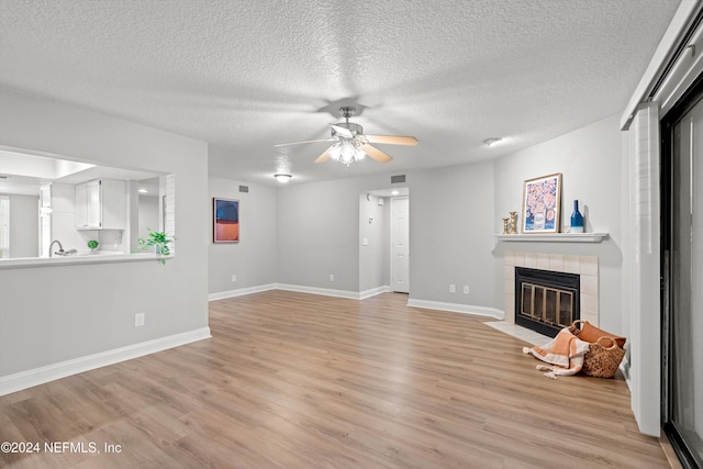 unfurnished living room with light wood-style flooring, a fireplace, baseboards, a ceiling fan, and a textured ceiling
