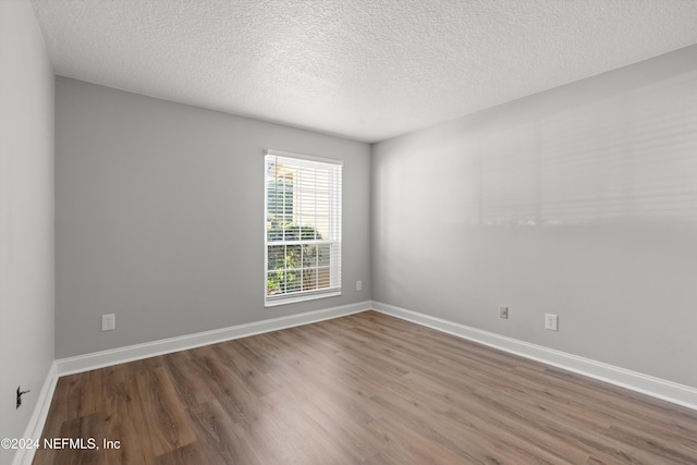 unfurnished room with wood finished floors, a textured ceiling, and baseboards