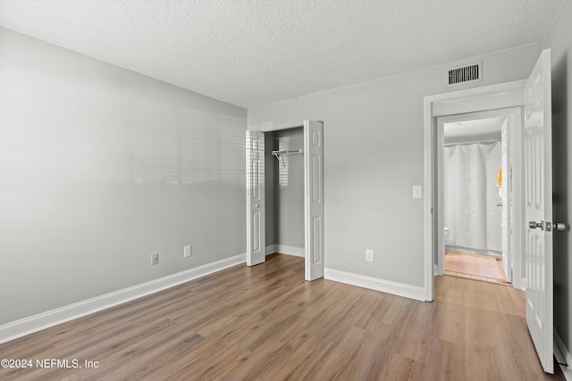 unfurnished bedroom with wood finished floors, a closet, a textured ceiling, and baseboards