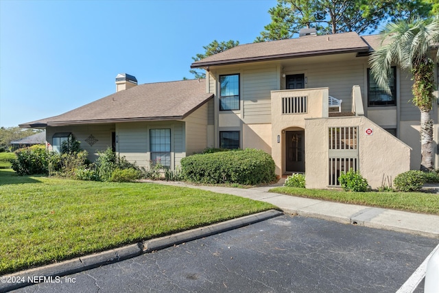 view of front of home with a chimney, a front lawn, and uncovered parking