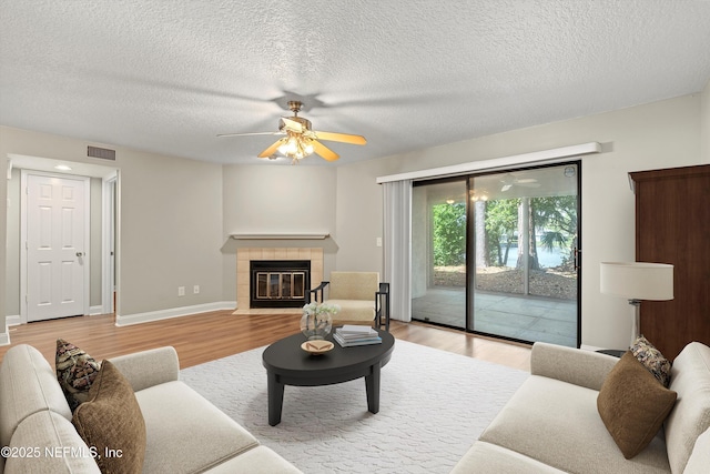 living area with light wood finished floors, a ceiling fan, a fireplace, a textured ceiling, and baseboards