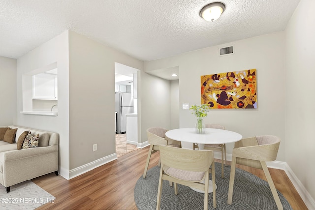 dining space with light wood-style floors, a textured ceiling, and baseboards