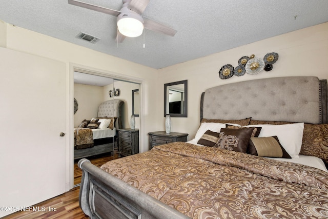 bedroom with a textured ceiling, a ceiling fan, wood finished floors, visible vents, and a closet