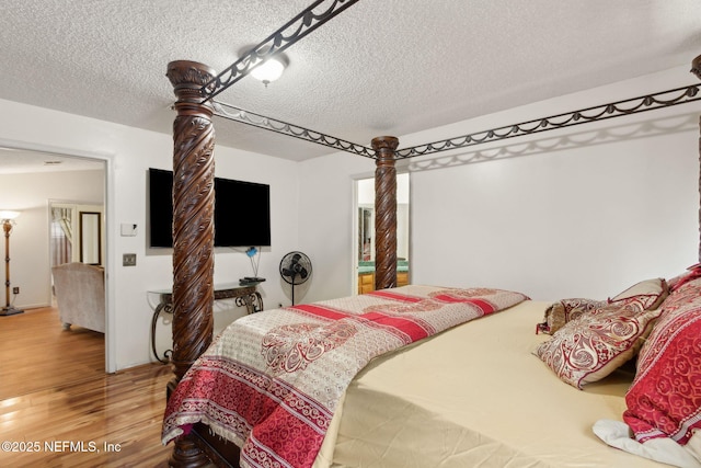 bedroom with light wood-type flooring, a textured ceiling, and ornate columns