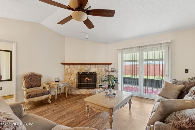 living room featuring a fireplace, light wood-style floors, a textured ceiling, a ceiling fan, and lofted ceiling
