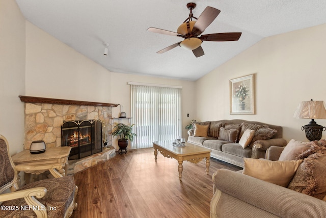 living area featuring a ceiling fan, wood finished floors, vaulted ceiling, and a fireplace