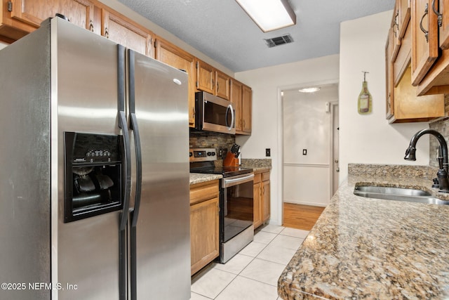 kitchen featuring a sink, stainless steel appliances, light tile patterned floors, backsplash, and visible vents