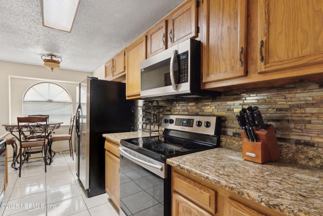 kitchen featuring light tile patterned floors, appliances with stainless steel finishes, tasteful backsplash, and brown cabinetry