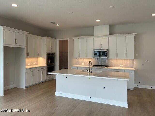 kitchen featuring tasteful backsplash, stainless steel microwave, light wood finished floors, double wall oven, and white cabinetry