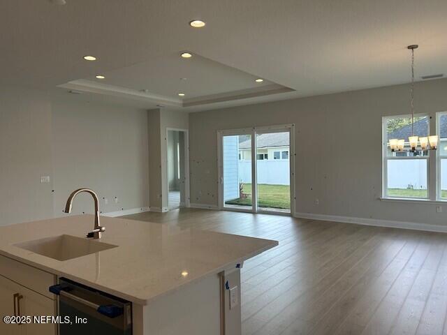 kitchen with a sink, a raised ceiling, dishwashing machine, and open floor plan