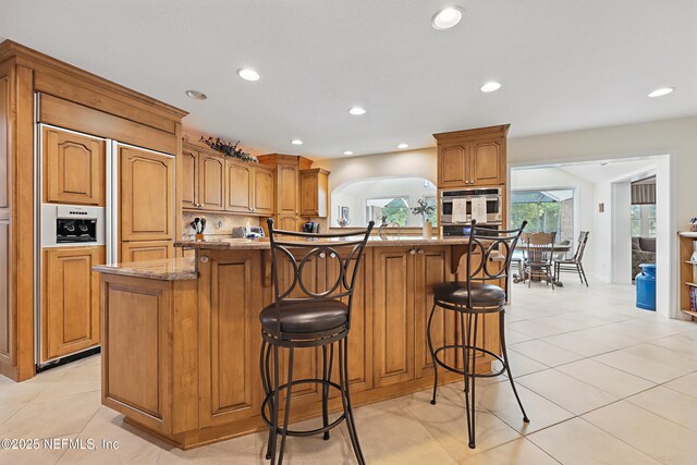 7805 Hunters Grove Rd, Jacksonville, FL 32256 - kitchen with paneled built in fridge, a breakfast bar area, recessed lighting, and brown cabinetry