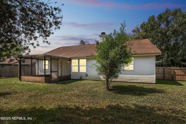 rear view of property featuring a lawn, a chimney, a sunroom, and a fenced backyard