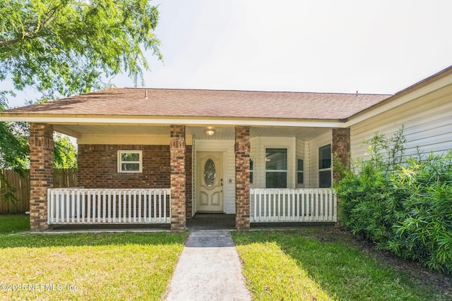view of front of home with a front yard, a shingled roof, and covered porch