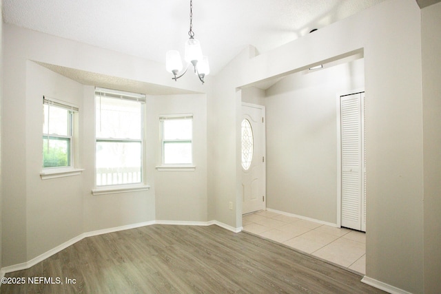 entryway featuring vaulted ceiling, a wealth of natural light, a chandelier, and wood finished floors