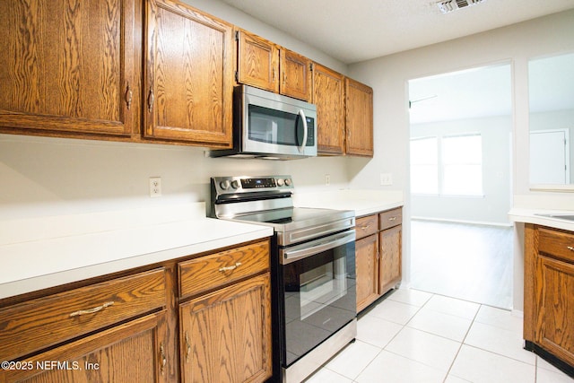kitchen featuring brown cabinetry, light tile patterned flooring, light countertops, and appliances with stainless steel finishes