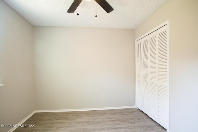 unfurnished bedroom featuring a closet, baseboards, a ceiling fan, and wood finished floors