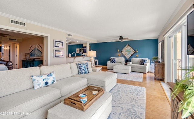 living area featuring visible vents, a ceiling fan, crown molding, and light wood-type flooring