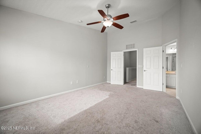 unfurnished bedroom featuring baseboards, light colored carpet, visible vents, and a towering ceiling