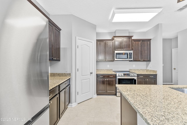 kitchen featuring visible vents, dark brown cabinets, baseboards, light stone counters, and stainless steel appliances