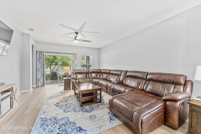 living room with ceiling fan, visible vents, baseboards, and light wood-type flooring