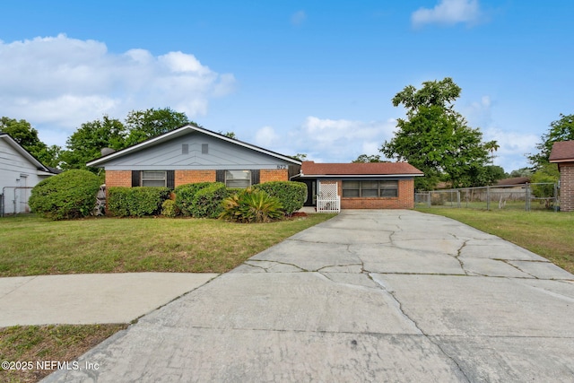 ranch-style home with concrete driveway, brick siding, fence, and a front lawn