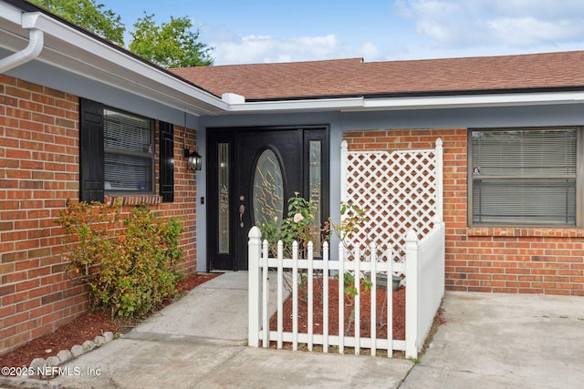 entrance to property with roof with shingles and brick siding