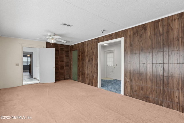 empty room featuring visible vents, carpet floors, ceiling fan, wooden walls, and a textured ceiling