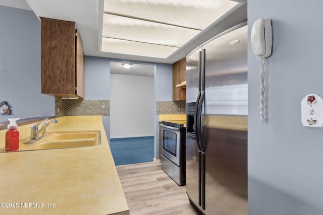 kitchen featuring a sink, light wood-style floors, light countertops, stainless steel appliances, and decorative backsplash