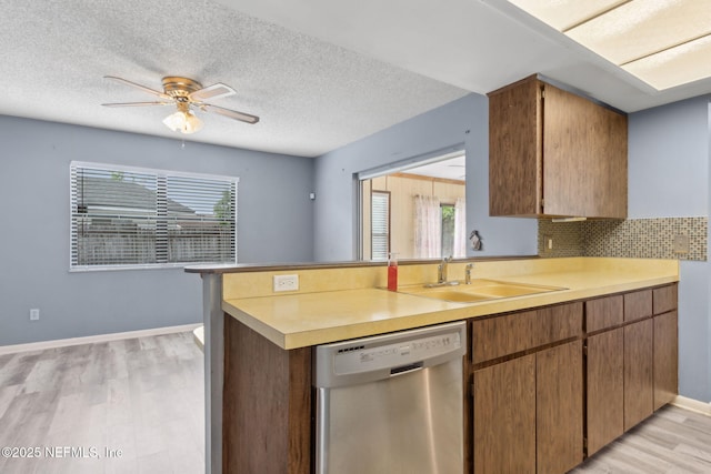 kitchen featuring stainless steel dishwasher, a sink, light wood-style floors, and light countertops
