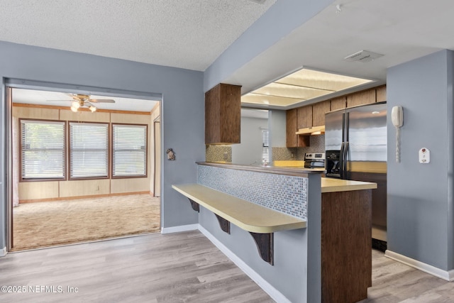 kitchen featuring ceiling fan, decorative backsplash, fridge with ice dispenser, light wood-type flooring, and visible vents