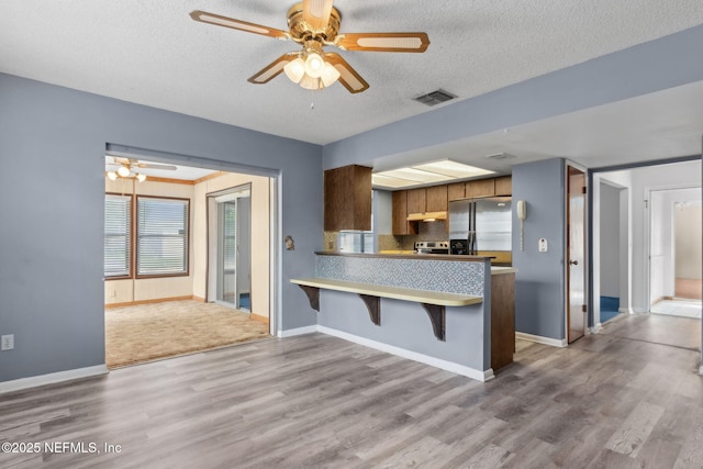 kitchen with stainless steel fridge with ice dispenser, a textured ceiling, a ceiling fan, wood finished floors, and visible vents