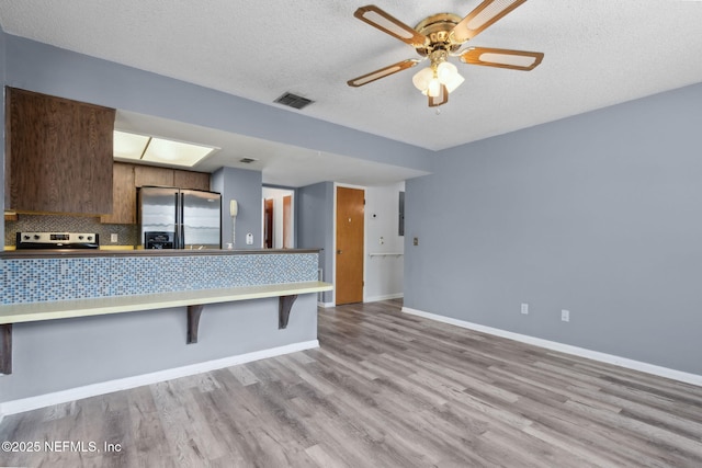 kitchen featuring appliances with stainless steel finishes, a kitchen breakfast bar, wood finished floors, backsplash, and visible vents