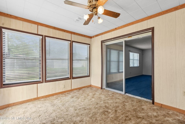carpeted spare room featuring baseboards, wood walls, and a ceiling fan