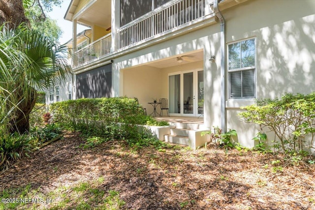 rear view of property with a ceiling fan, french doors, a balcony, and stucco siding