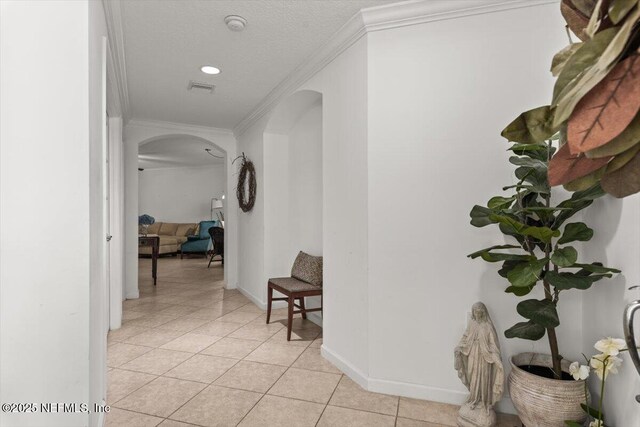 corridor featuring visible vents, crown molding, arched walkways, light tile patterned floors, and baseboards