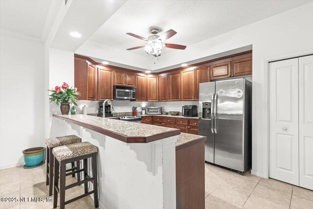 kitchen featuring ceiling fan, a breakfast bar, stainless steel appliances, a peninsula, and light tile patterned floors