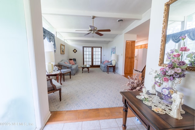 living area with a ceiling fan, beamed ceiling, and light colored carpet