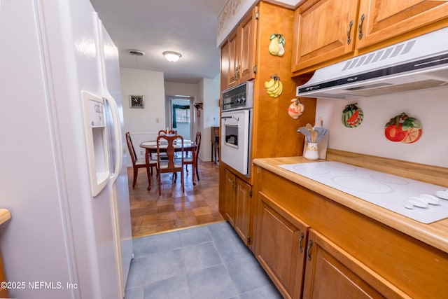 kitchen with under cabinet range hood, brown cabinetry, white appliances, and light countertops
