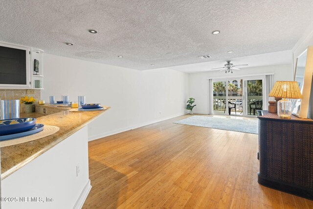 living room with a textured ceiling, ceiling fan, light wood-style floors, baseboards, and recessed lighting