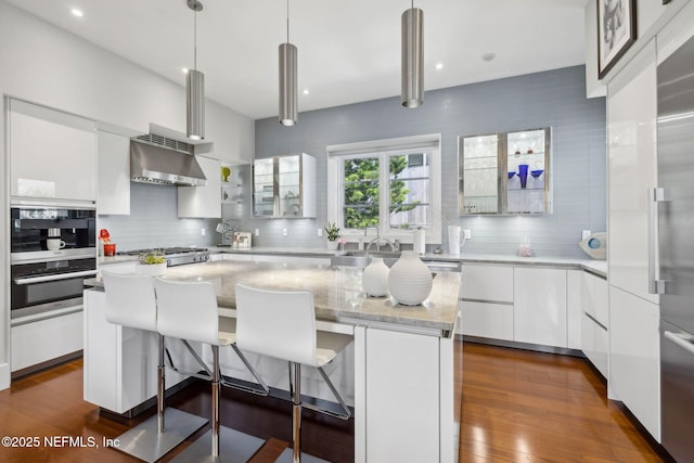 kitchen featuring a center island, white cabinetry, backsplash, and exhaust hood