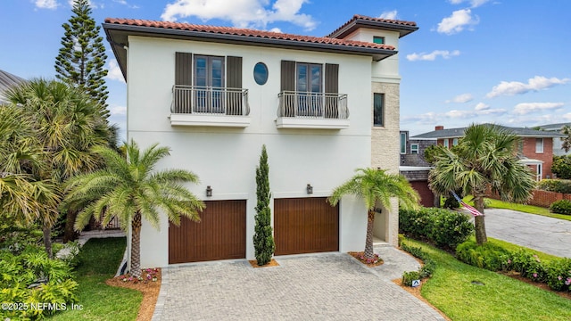 mediterranean / spanish-style home with an attached garage, decorative driveway, stucco siding, and a balcony