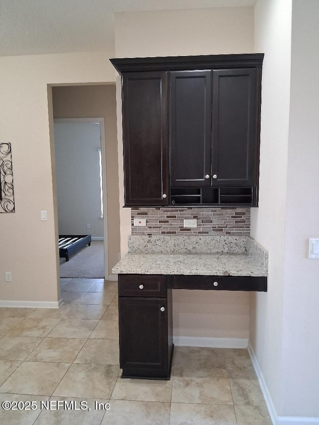 kitchen featuring baseboards, decorative backsplash, light tile patterned floors, and light stone counters