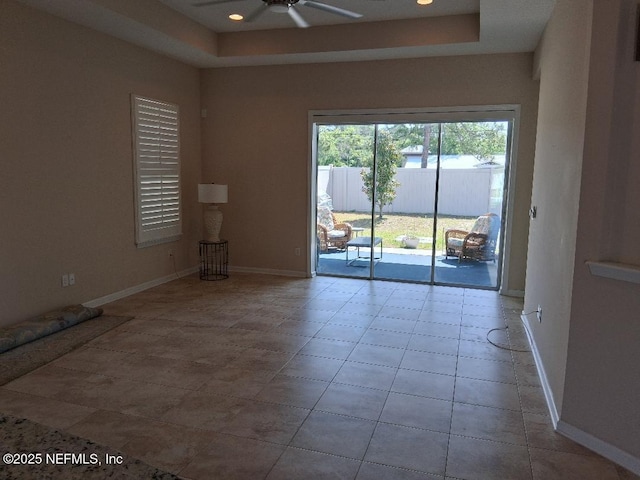 tiled spare room featuring a raised ceiling, baseboards, and a ceiling fan
